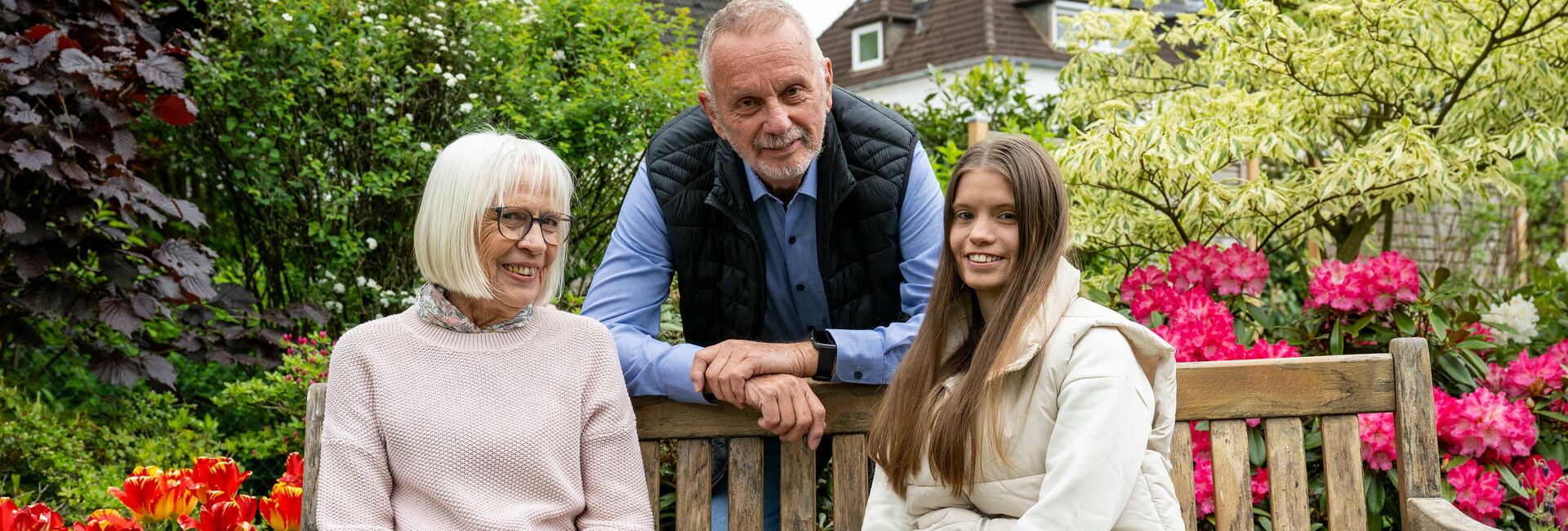 Betreutes Wohnen in Familien BWF Bethel.regional Bielefeld Gastmutter und junge Frau sitzen auf einer Bank im Garten, der Gastvater steht zwischen den beiden hinter der Bank