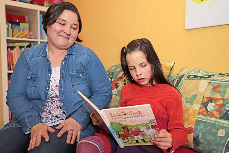 Eine Frau sitzt mit einem Mädchen, das ein Buch liest, auf dem Sofa