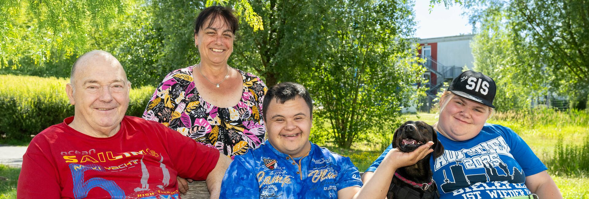 Gasteltern mit einem zu betreuenden jungen Mann und Hund im Garten auf einer Gartenbank