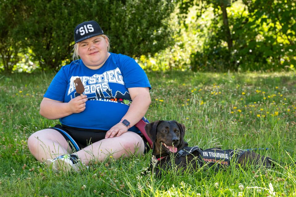 Eine junge Frau mit Hund sitzt im Garten auf dem Rasen und isst ein Eis am Stiel